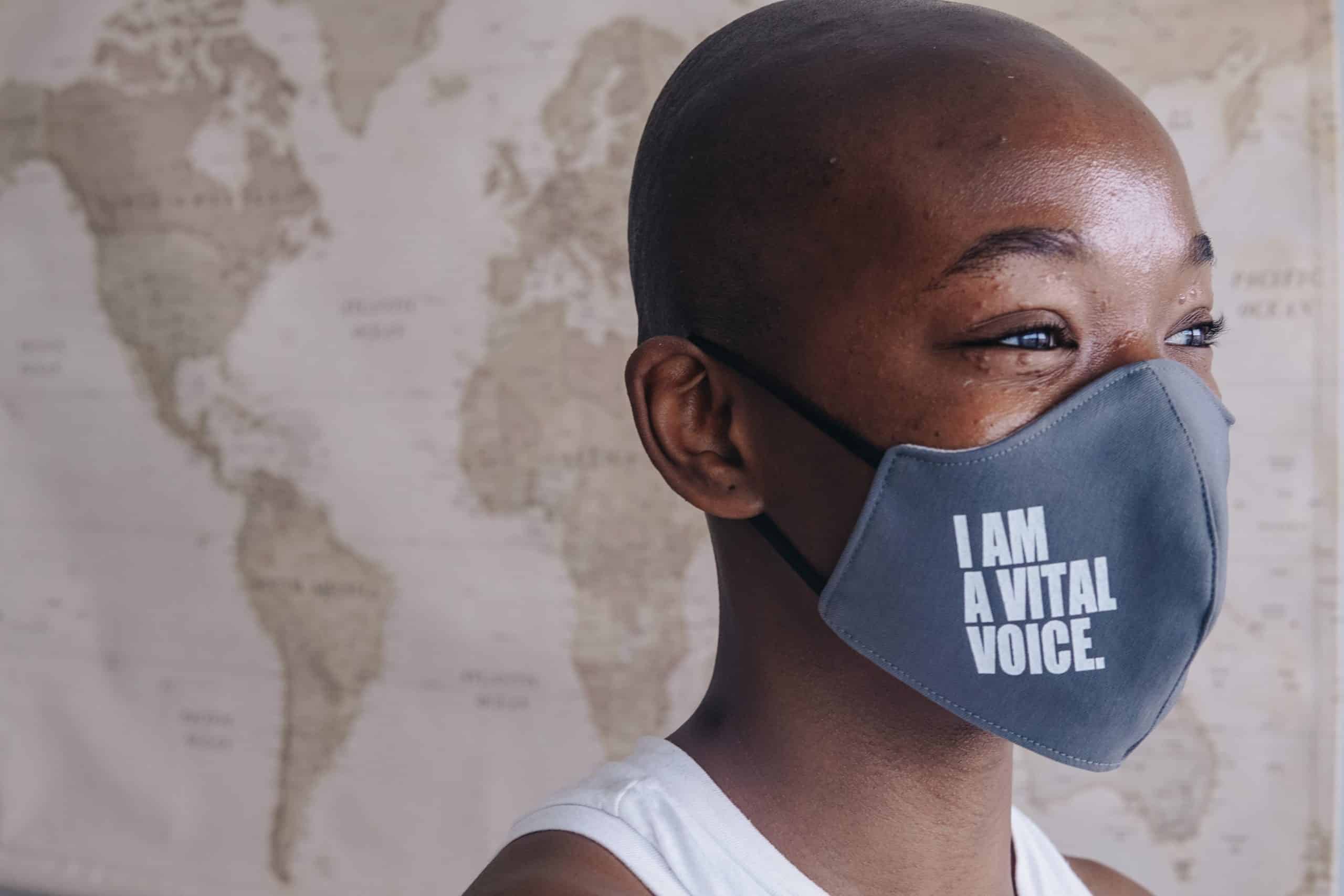 Woman wears a gray face mask that reads "I am a Vital Voice" across the side.
