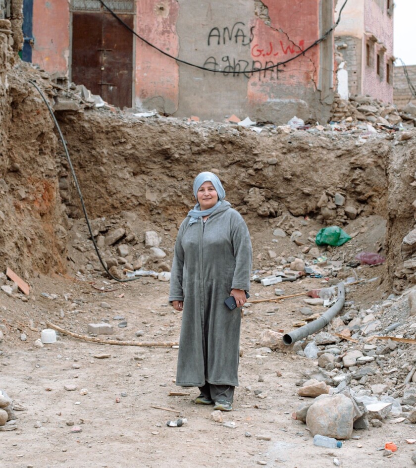 Woman in gray clothing standing among rubble.