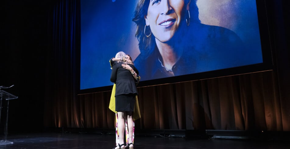 A heartfelt embrace on stage, celebrating recognition and shared purpose.