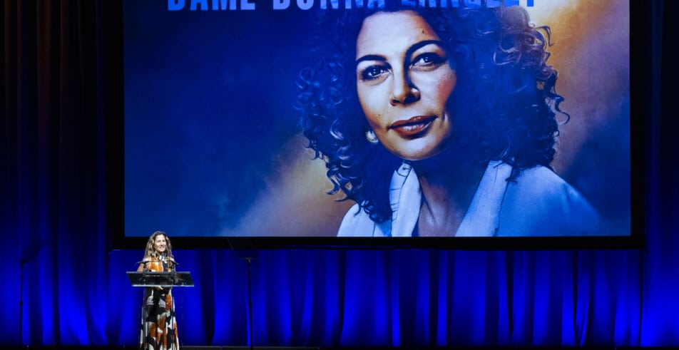 Ariela Suster, presenter of the 2026 Global Leadership Award, introduces the award's honoree against a backdrop naming Dame Donna Langley, the honoree.