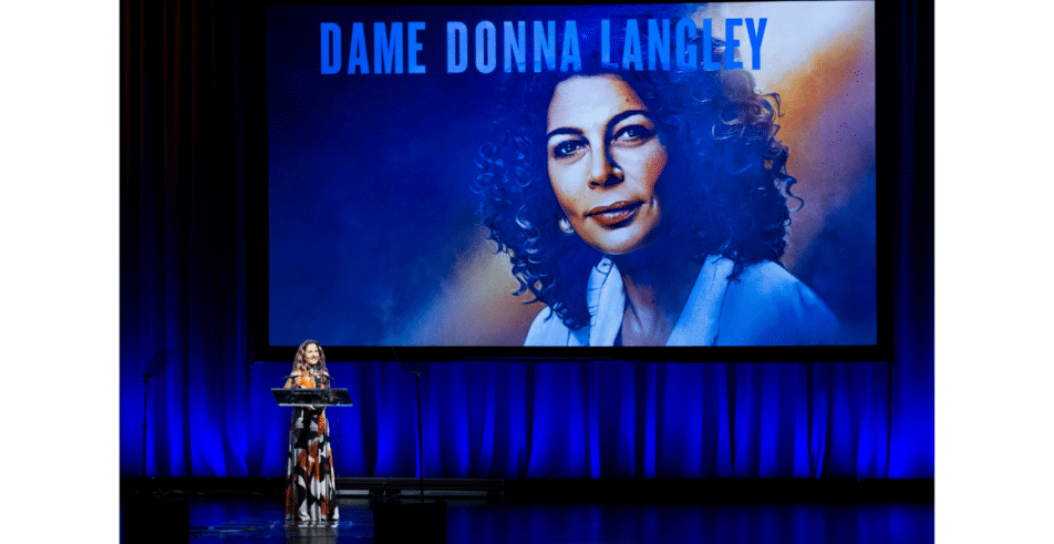 Ariela Suster, presenter of the 2026 Global Leadership Award, introduces the award's honoree against a backdrop naming Dame Donna Langley, the honoree.