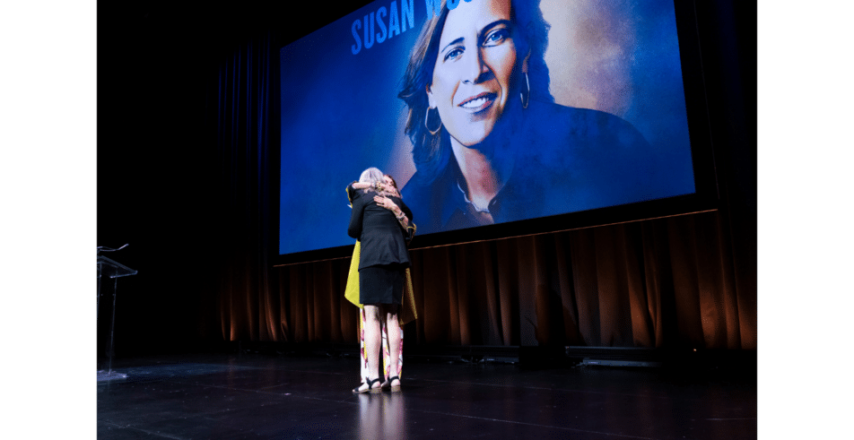 A heartfelt embrace on stage, celebrating recognition and shared purpose.